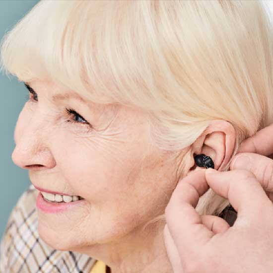 Frau beim Einsetzen eines Hörgeräts.