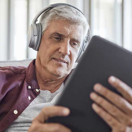 Mann mit Kopfhörern blickt in Tablet.